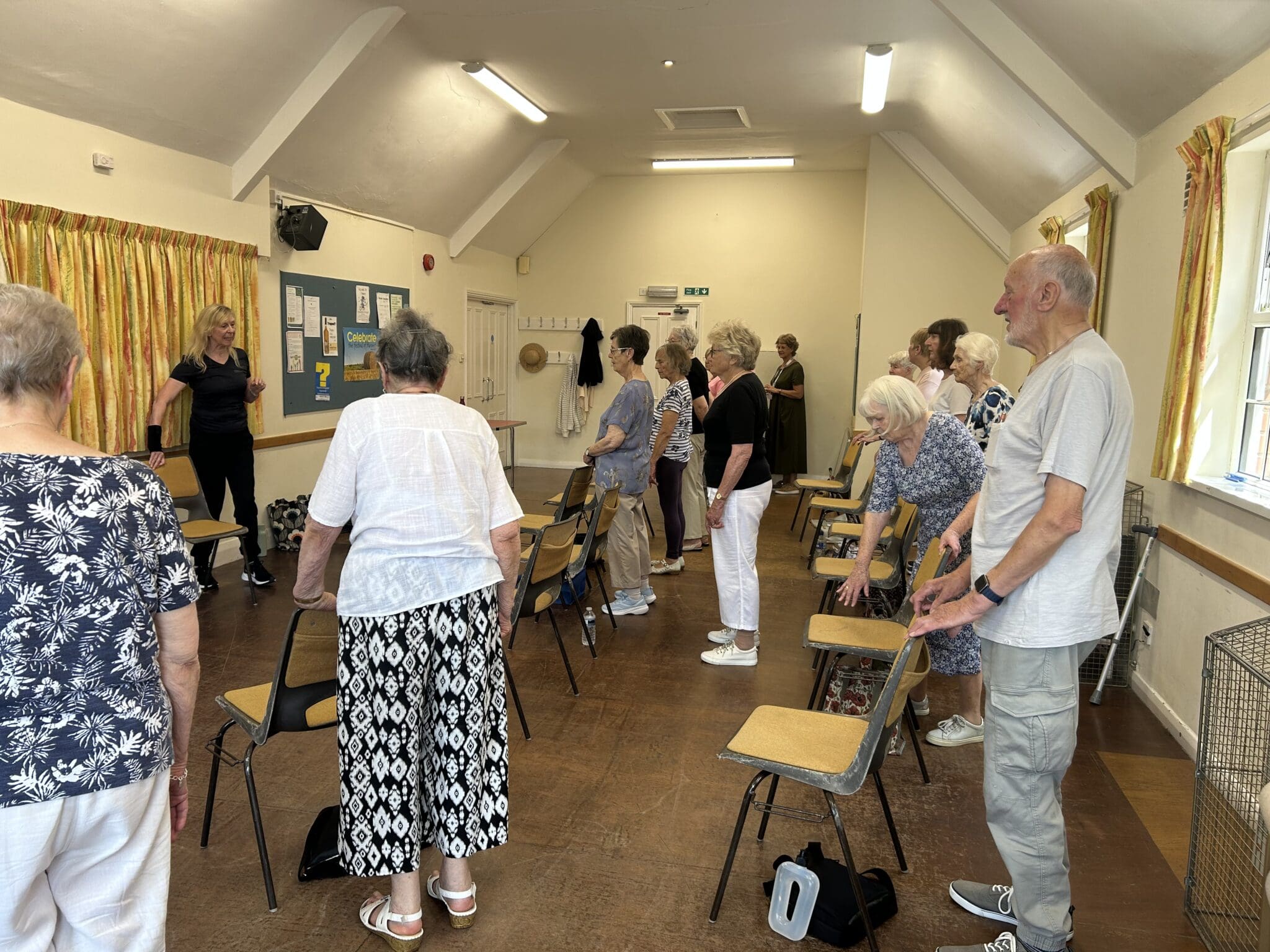 A group of seniors in a room standing with chairs as they participate in an exercise class