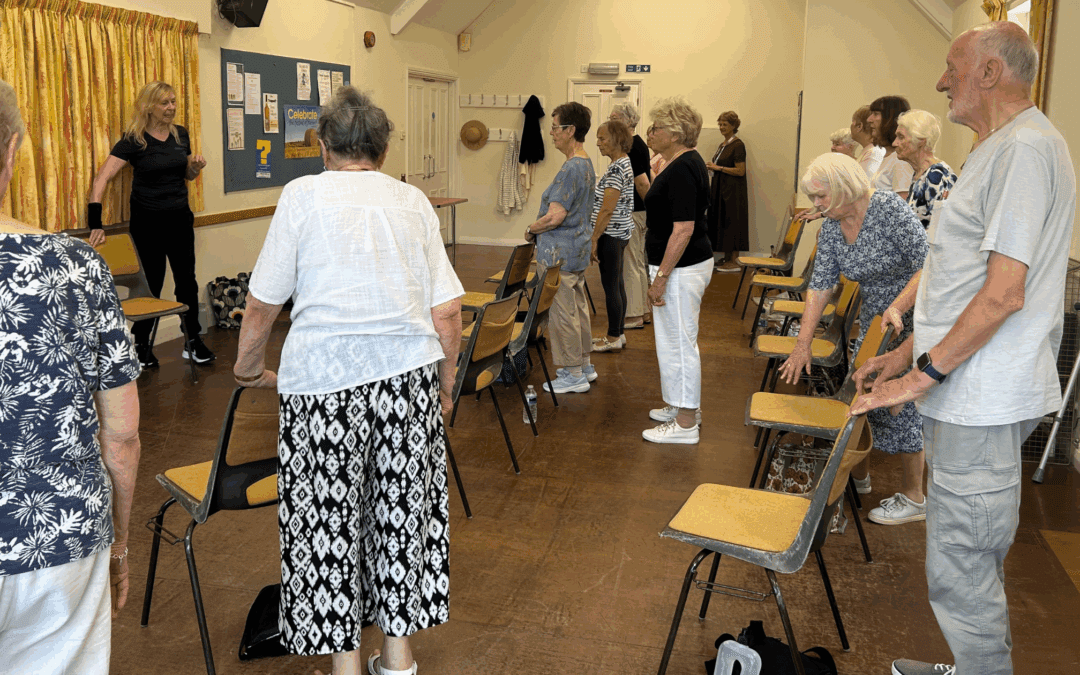 A group of seniors in a room standing with chairs as they participate in an exercise class